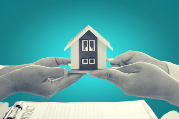 Dos personas se entregan una maqueta de casa sobre un contrato de compraventa