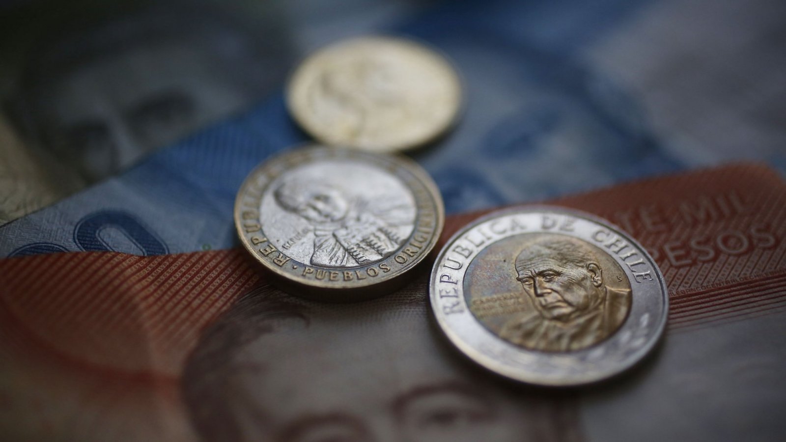 Monedas chilenas de 100 y 500 pesos sobre billetes de mil y veinte mil pesos, como el dinero que ahorra el subsidio a la tasa en el dividendo