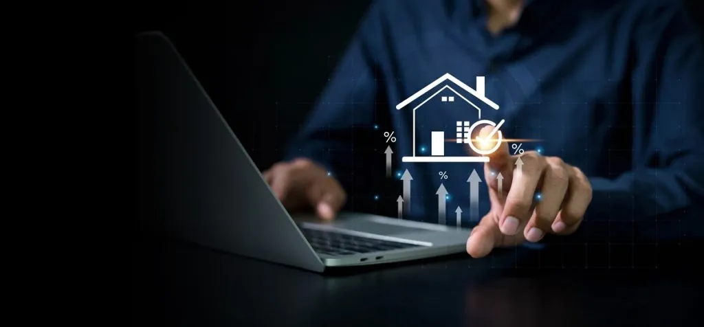 Persona en un notebook tocando el ícono de una casa rodeado de flechas y porcentajes al alza, como en una inversión inmobiliaria